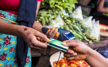 close up of an african woman selling in a local african market holding a mobile point of sale device collecting a credit card from a customer traitement-bancaire-sécurisé
